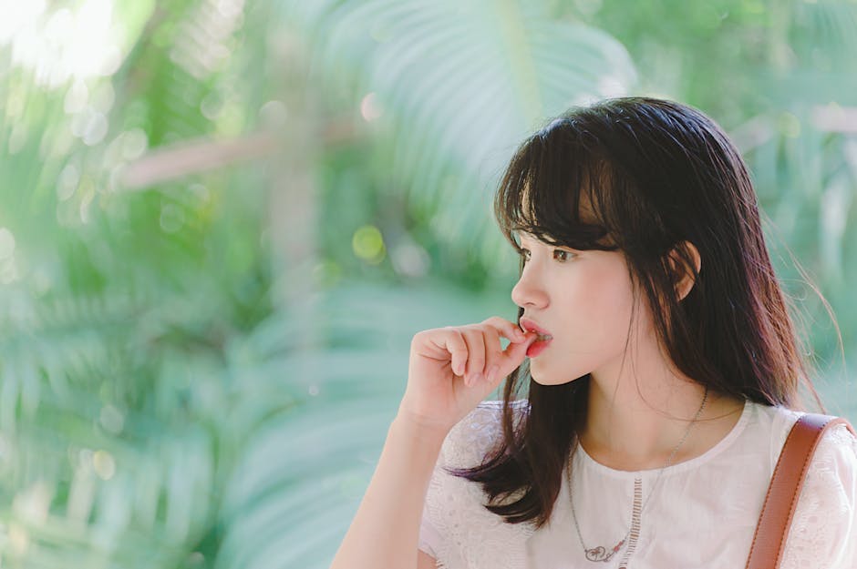 A young woman deep in thought surrounded by vibrant green foliage on a sunny day.