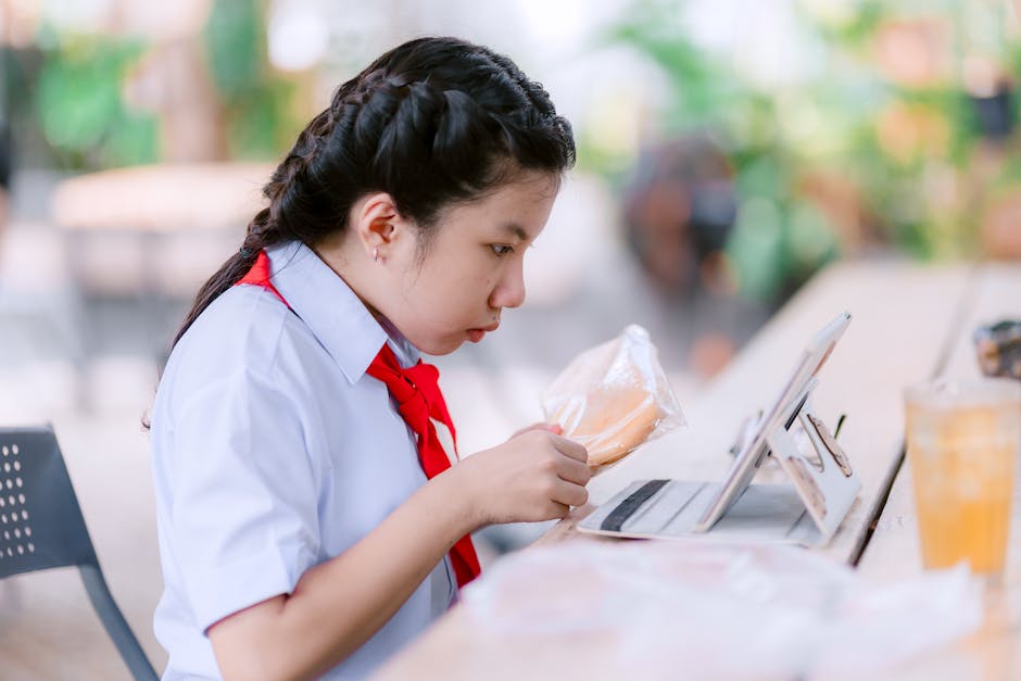 Concentrated student in uniform studying on a tablet at an outdoor cafe setting.