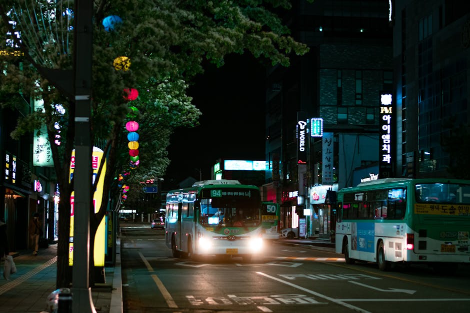 Urban street at night with illuminated buses and colorful neon lights.