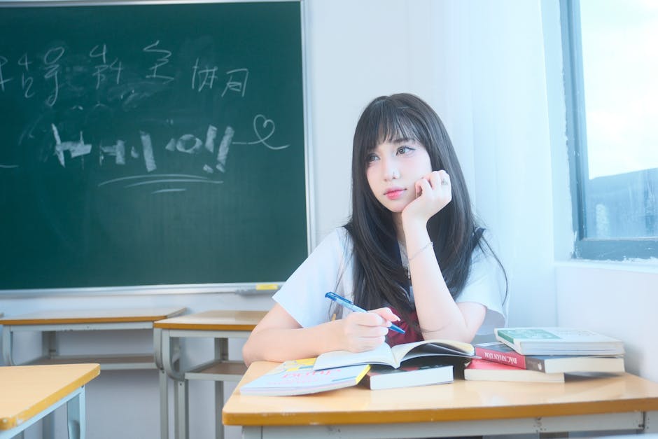 A young woman studying in a bright classroom with numerous books and a chalkboard.