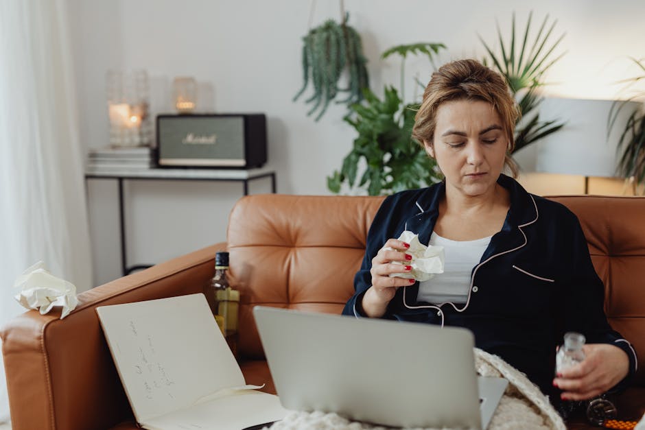 Woman in pajamas sitting on sofa with laptop and drink, surrounded by cozy home decor.