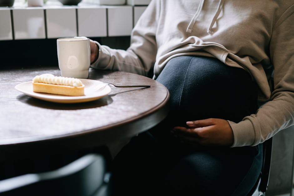 A close-up of a pregnant woman sipping coffee and enjoying a pastry indoors.