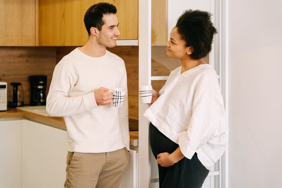 A happy expectant couple enjoying a conversation in the kitchen with coffee mugs.