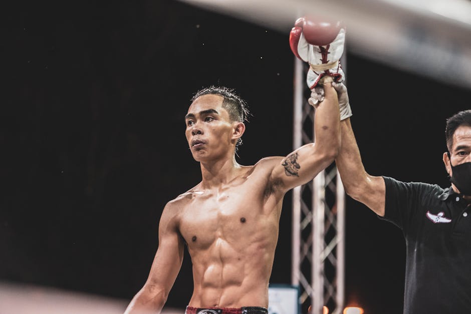A skilled boxer raises his hand in triumph after a successful match under bright lights.