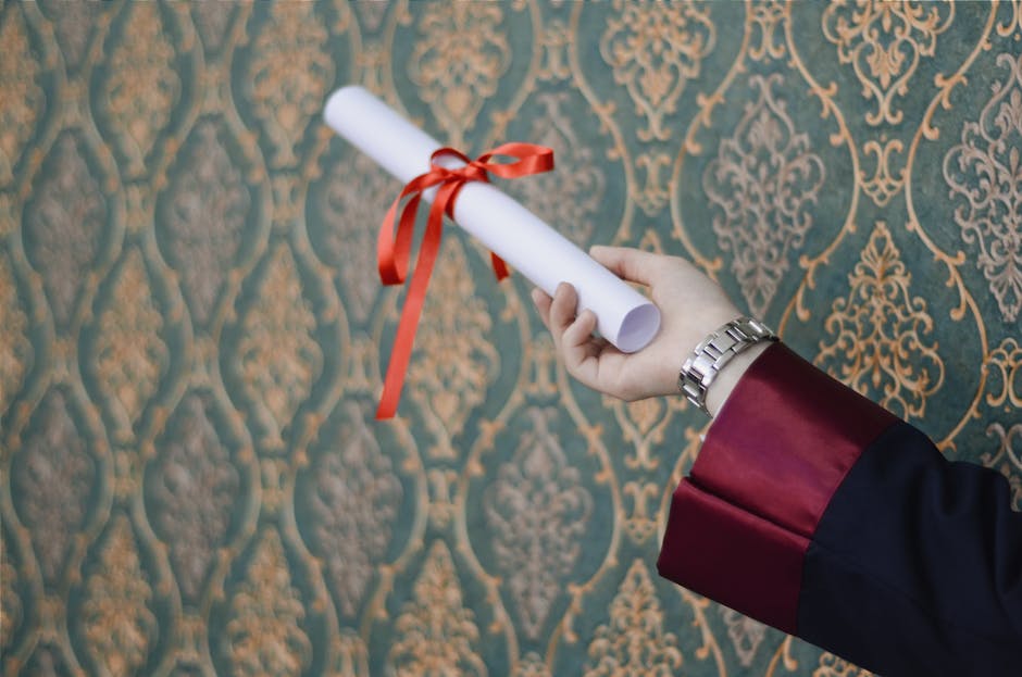 A graduate's hand holding a diploma with red ribbon, symbolizing achievement.