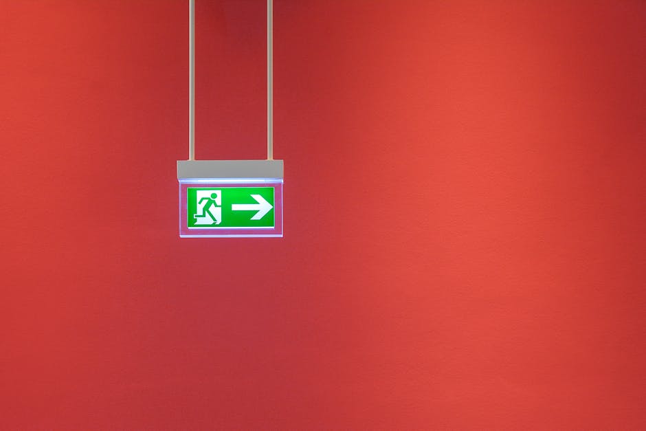 Green emergency exit sign with arrow on vibrant red wall, indicating direction for safety.
