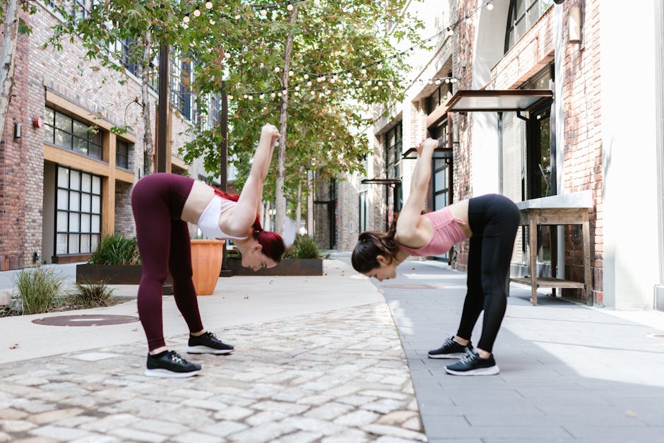 Two women performing flexibility exercises outdoors in an urban street setting.