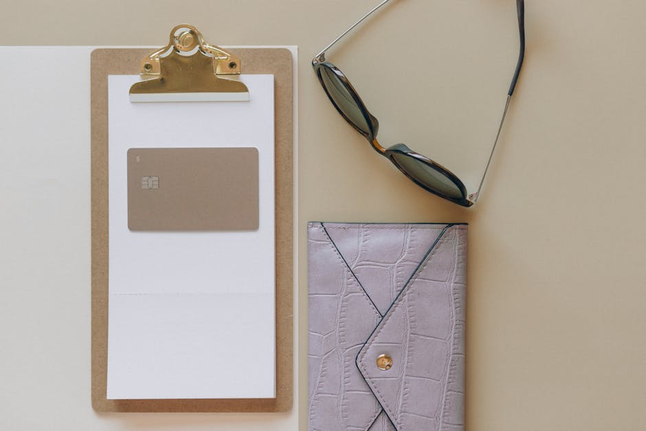 Flat lay image featuring a wallet, sunglasses, card, and clipboard on a beige surface.