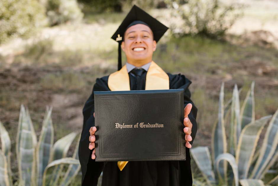 Smiling graduate in academic dress displaying diploma outdoors, symbolizing achievement.