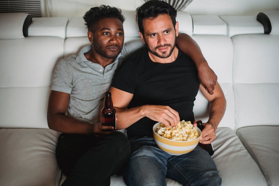 A loving interracial couple enjoying a movie night on the sofa with popcorn and drinks.