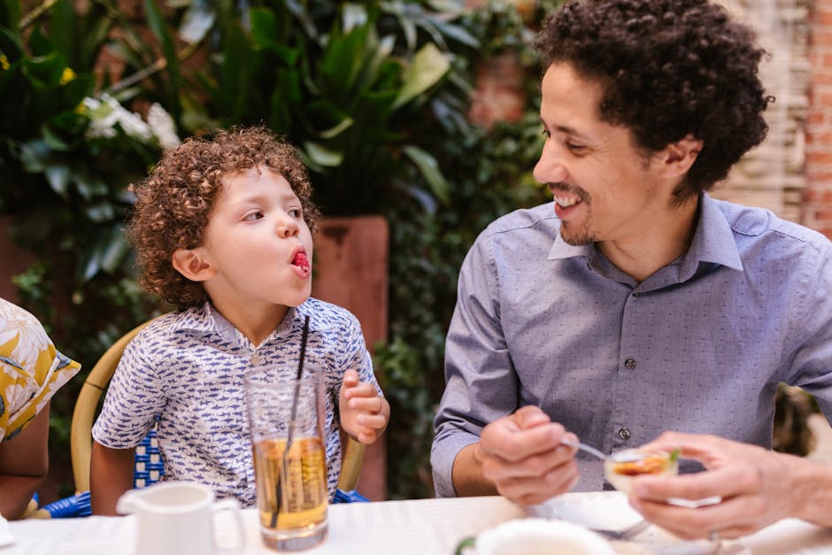 Father and son share a joyful moment while dining outdoors, capturing playful expressions.