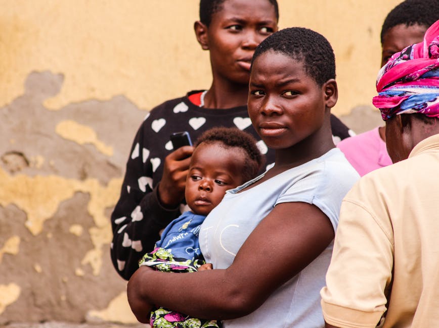 A powerful portrait of a mother holding her baby with others in a city environment.