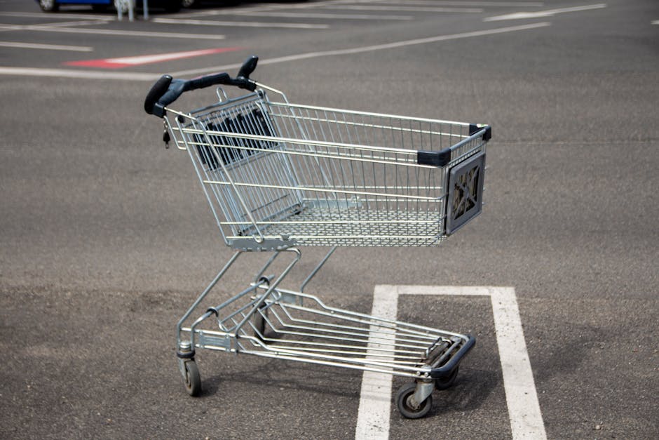 A lone shopping cart sits idle in an empty parking lot on a sunny day.