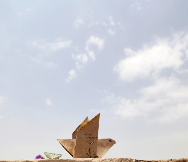 Origami bird on a ledge against a bright sky, showcasing minimalist art and creativity.