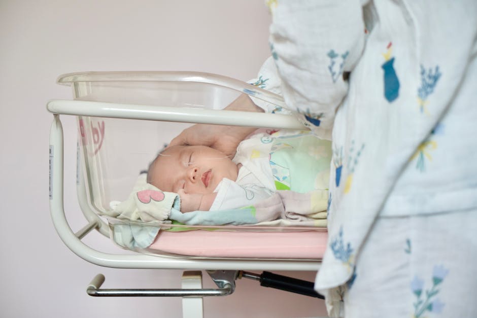 A tender moment of a newborn baby sleeping peacefully in a hospital bassinet being gently touched by a parent.