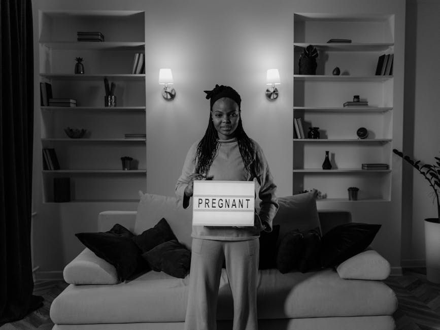 Black and white portrait of a pregnant woman holding a light box indoors.