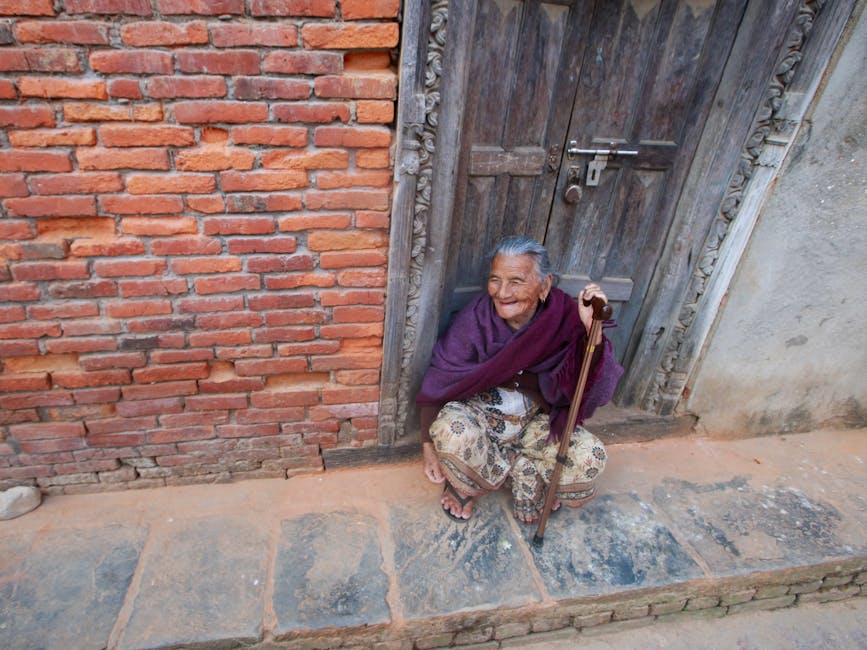 Portrait of an elderly woman sitting by a rustic brick wall and carved wooden doorway.