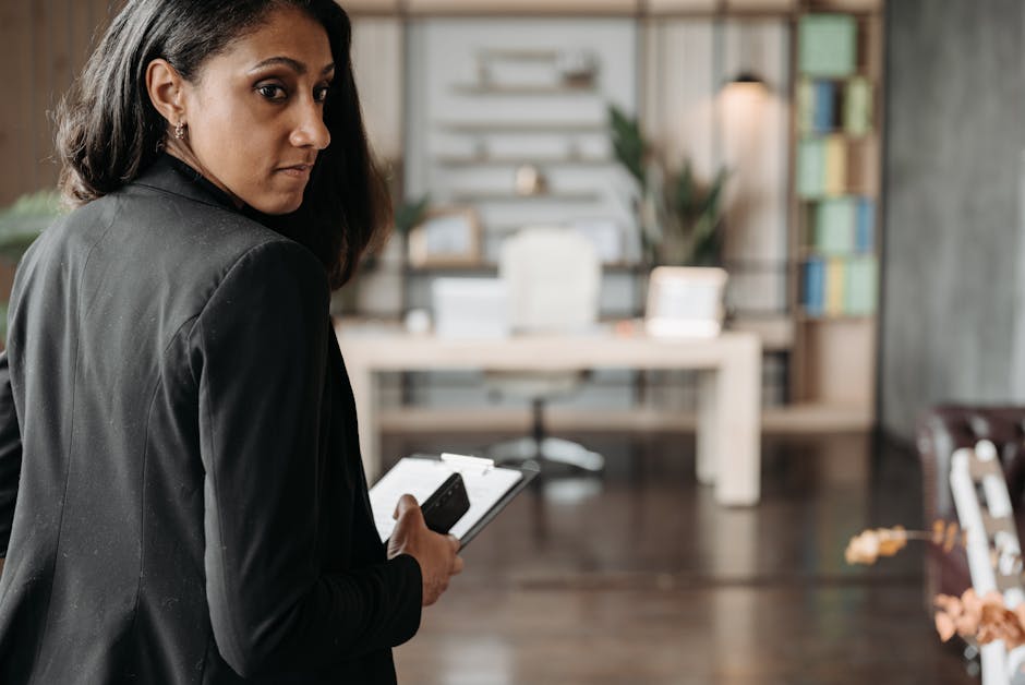 Confident businesswoman in a black suit holding a phone in a chic office interior.