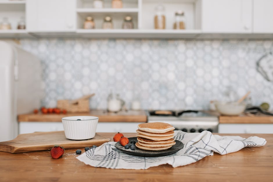 Cozy kitchen scene with pancakes, blueberries, and strawberries on a wooden table.