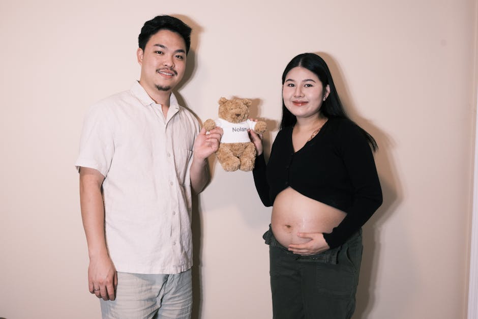 Expecting couple holding teddy bear with baby's name, celebrating joyfully indoors.