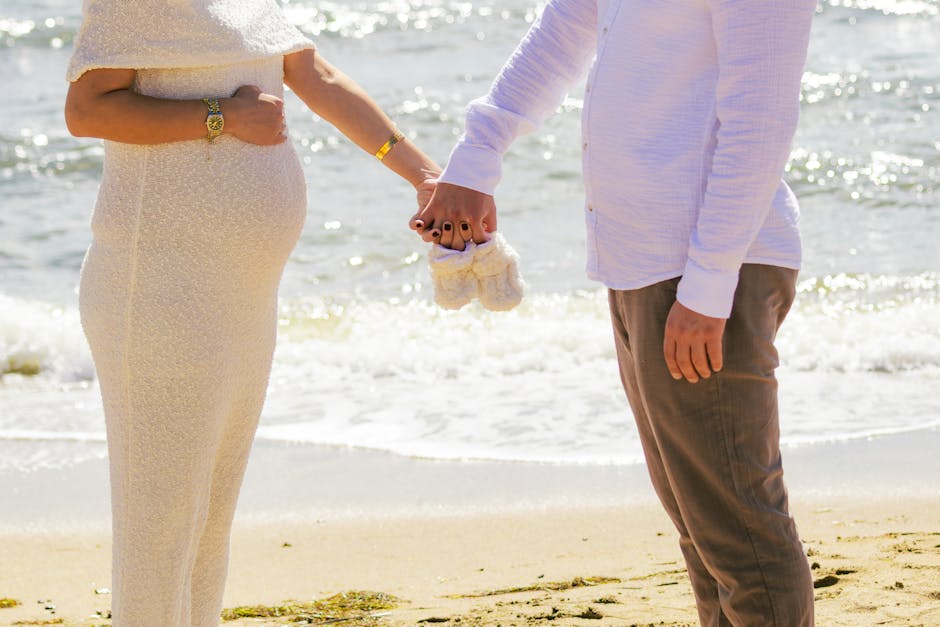 Pregnant couple holding baby shoes on a sunny beach in Balıkesir, Türkiye.