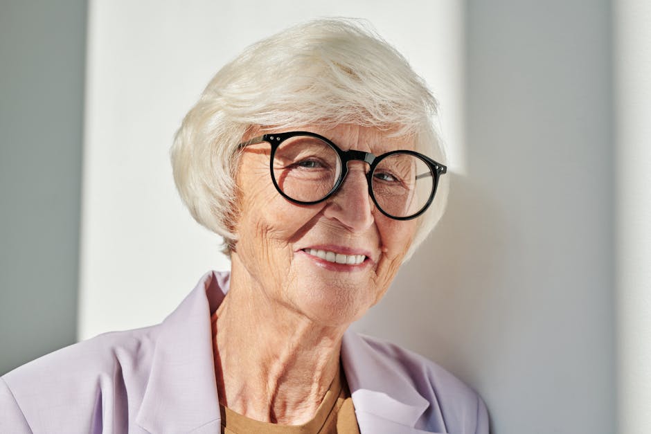 Close-up portrait of a smiling senior woman with glasses enjoying the sunlight indoors.