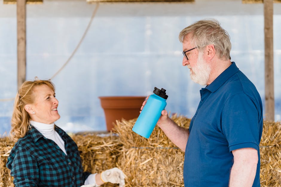Elderly man and woman in a casual conversation indoors with a blue tumbler. Haystack in the background.