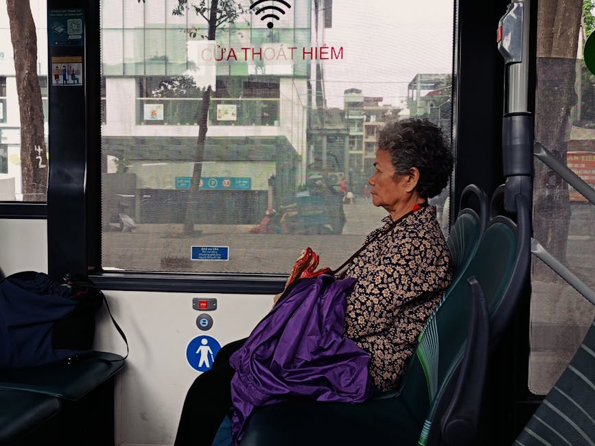 Elderly woman seated on a city bus, reflecting on urban life during a daytime commute.