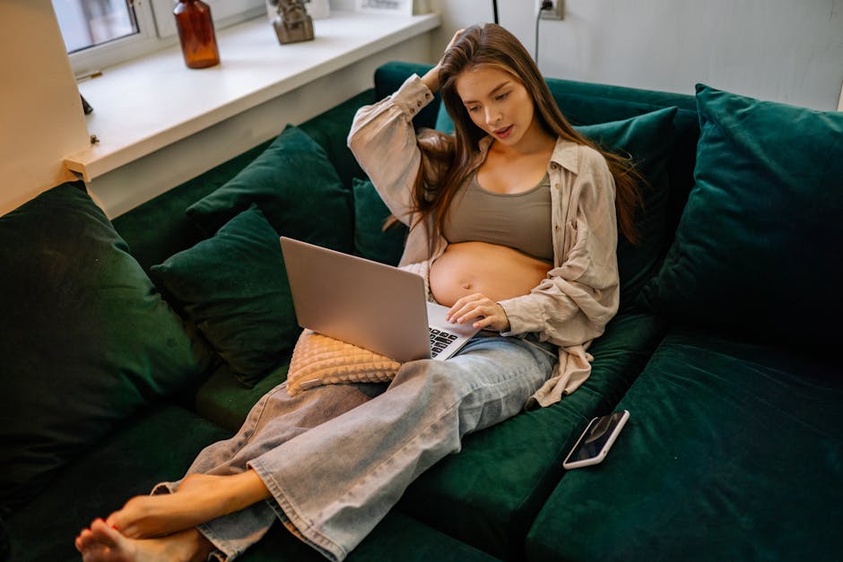 Pregnant woman relaxing on a couch, using a laptop, represents comfort and modern lifestyle.