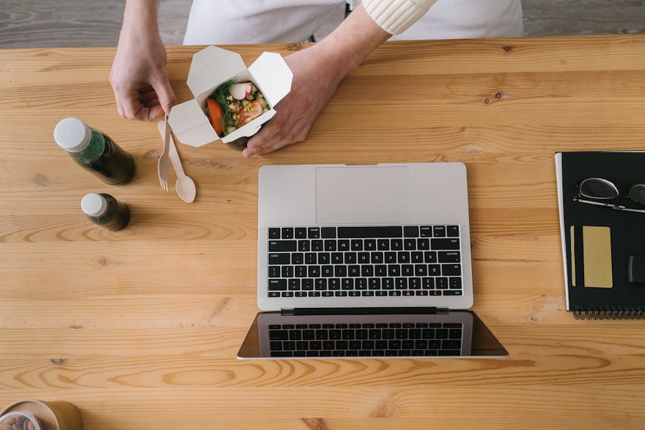 A top-down view of a desk with a laptop and healthy takeout meal in a serene workspace.