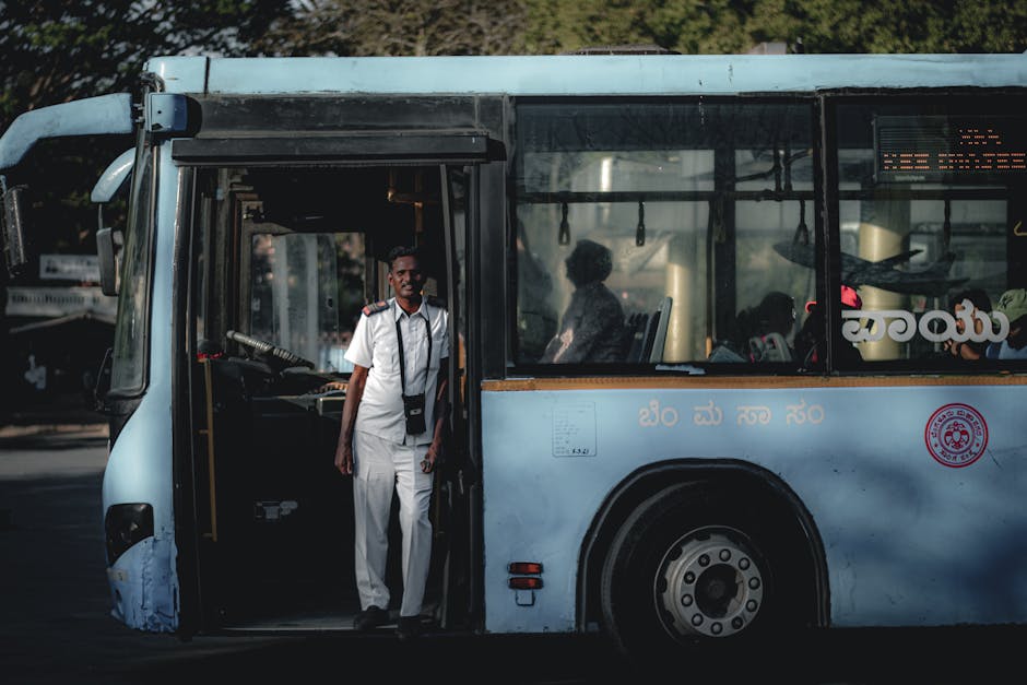 Bus driver wearing a white uniform standing by the bus door, sunlight casting shadows inside