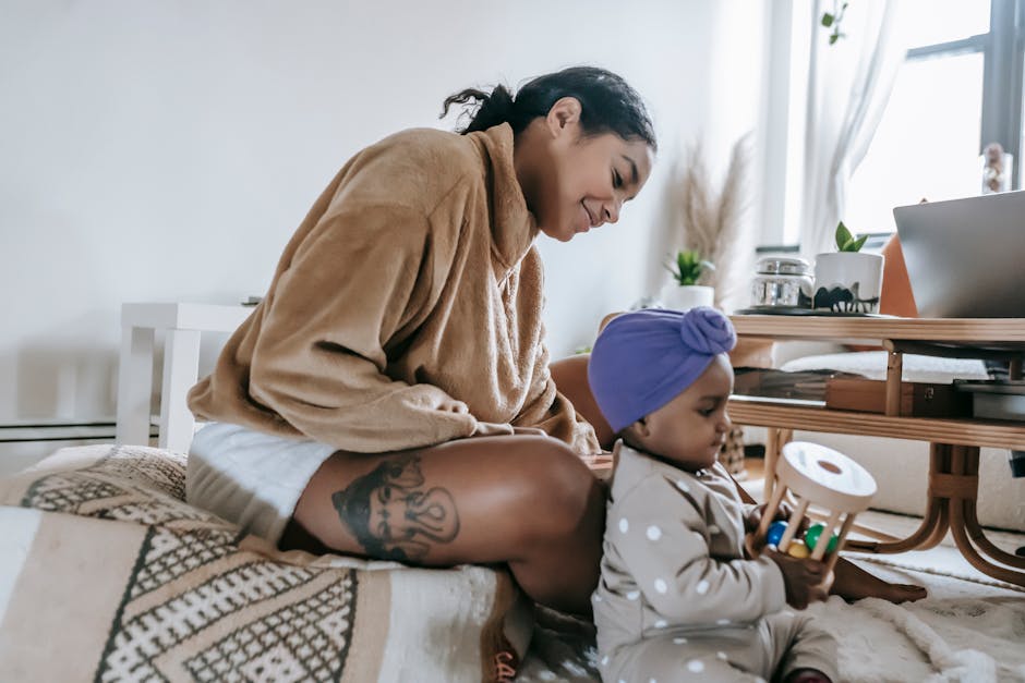 Side view of positive African American mother sitting near black little daughter with wooden toy in living room at home