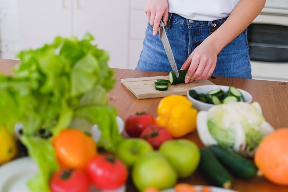 Woman slicing cucumbers surrounded by fresh produce in a bright kitchen setting.