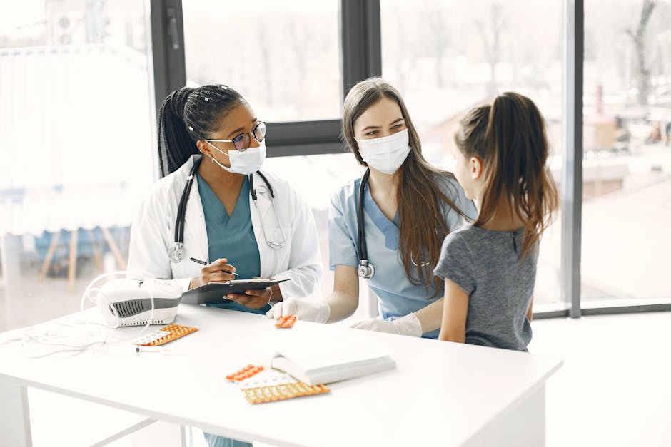 Two female doctors in masks assist a child in a bright medical room.