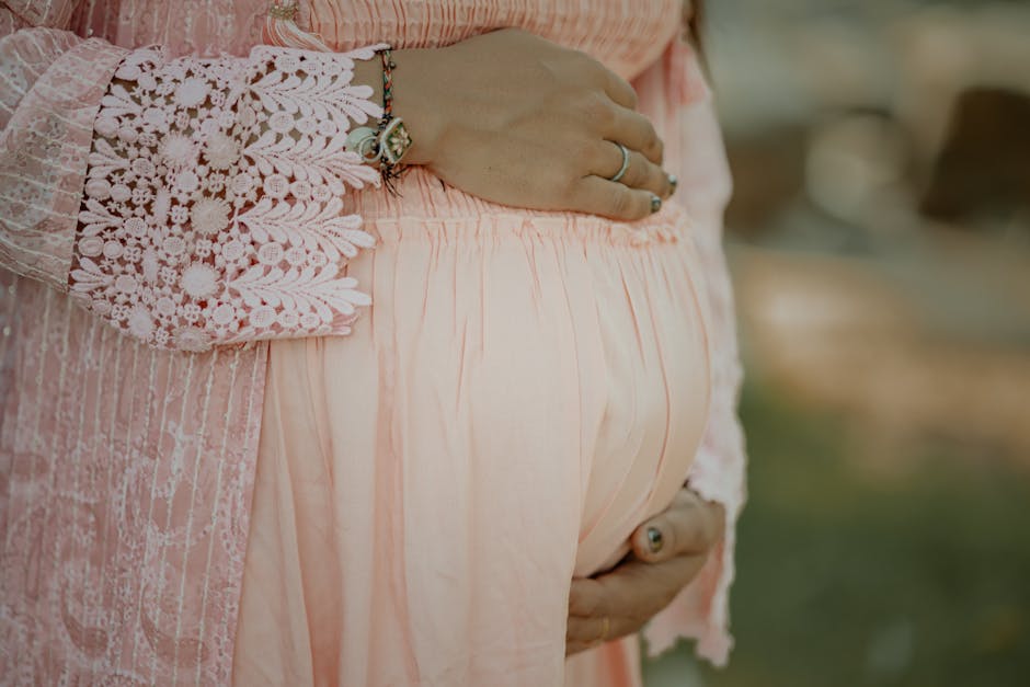Close-up of a pregnant woman embracing her belly in a delicate pink dress.