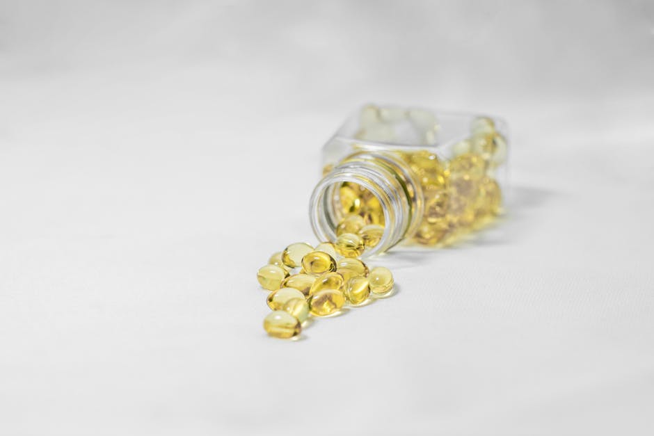 Close-up of yellow softgel capsules spilled from a glass bottle on a white surface.