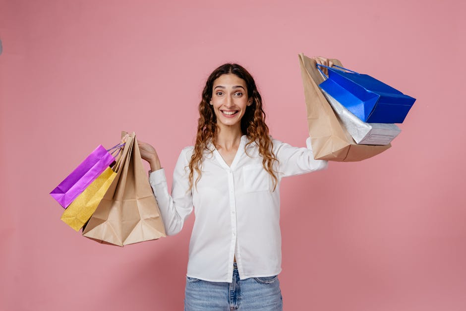 Cheerful woman holding various shopping bags against a pink background, expressing joy.