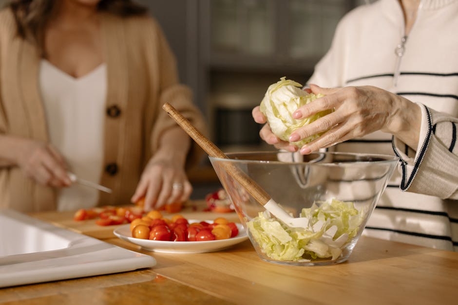 Two women chopping fresh vegetables for a salad in a modern kitchen setting.
