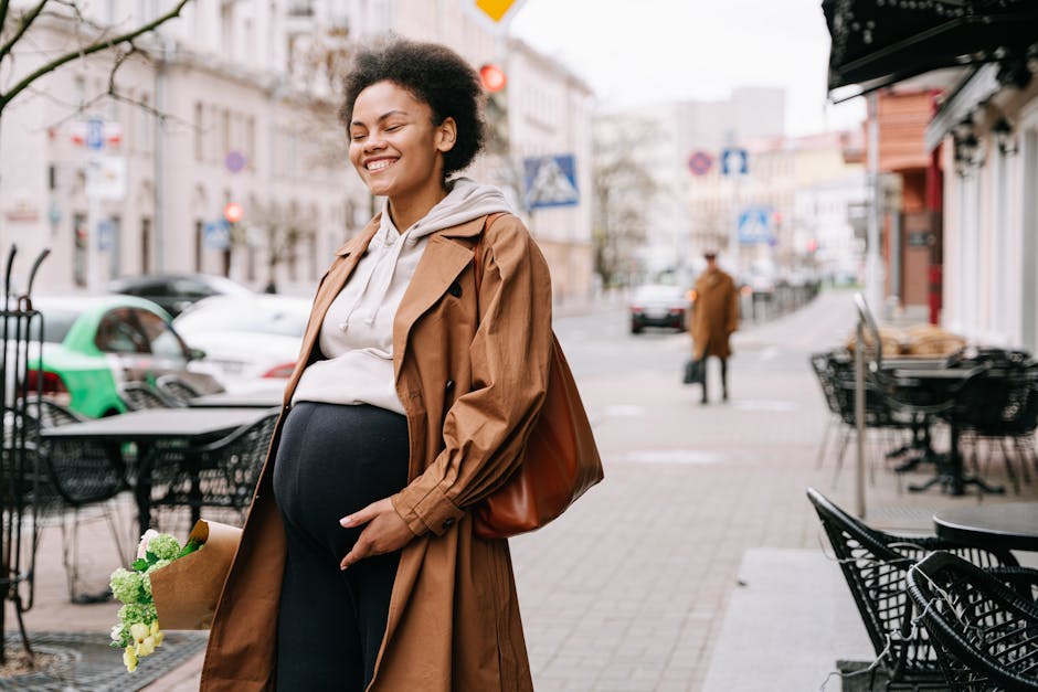 A joyful pregnant woman walking on a city street, holding a bouquet of flowers and smiling.