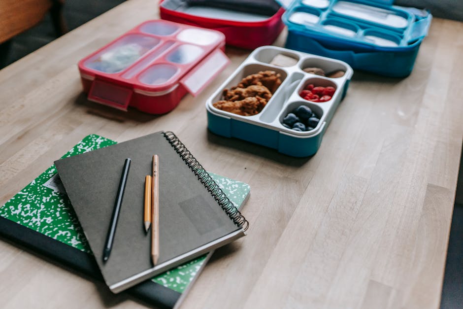 High angle of various containers with food behind notebooks and pencils on wooden table