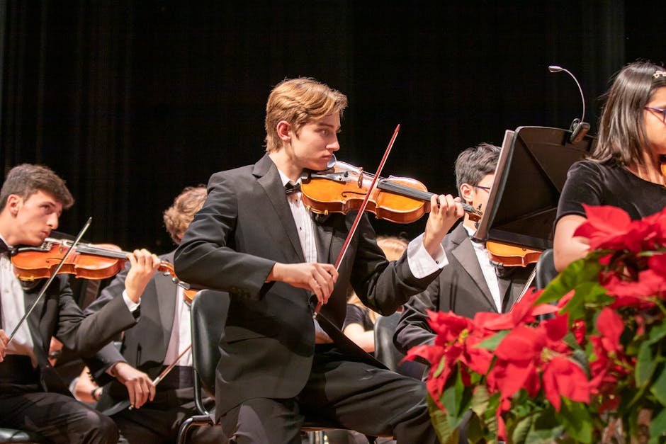 A group of young musicians performing in a live orchestra with violins.