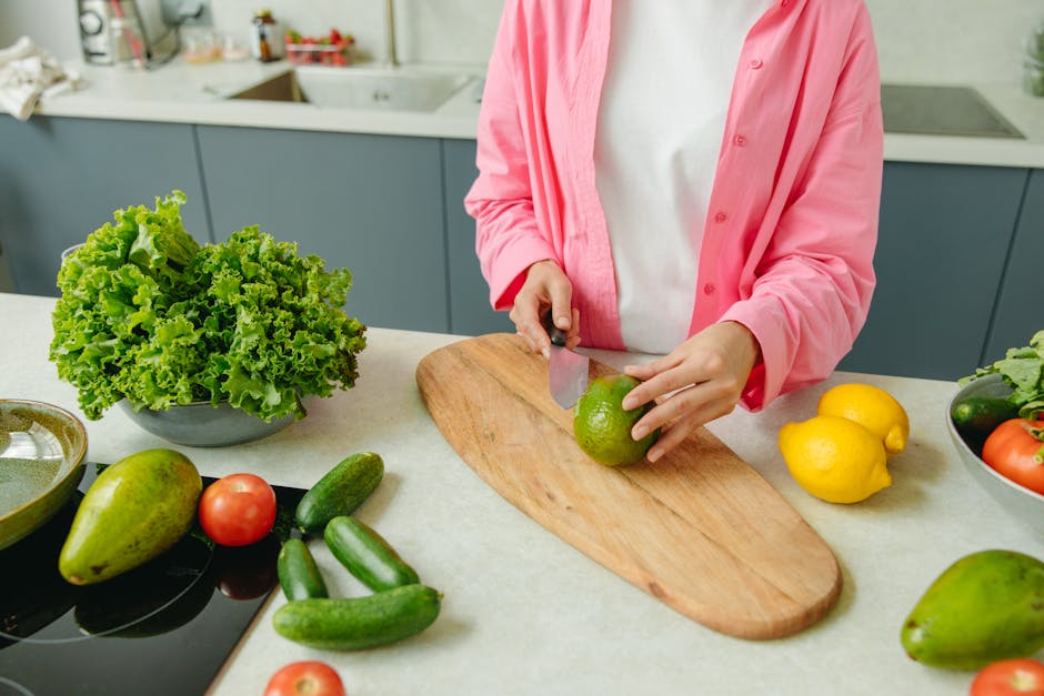 Person in pink shirt chopping vegetables on a wooden board, surrounded by fresh produce.