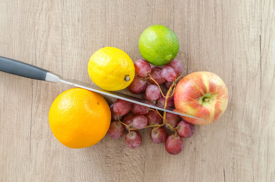 A vibrant assortment of fresh fruits includes apple, grapes, orange, lime, and lemon, arranged with a knife on a wooden surface.