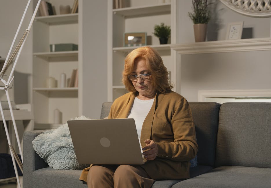 Senior woman with eyeglasses working on a laptop in a cozy living room setting.