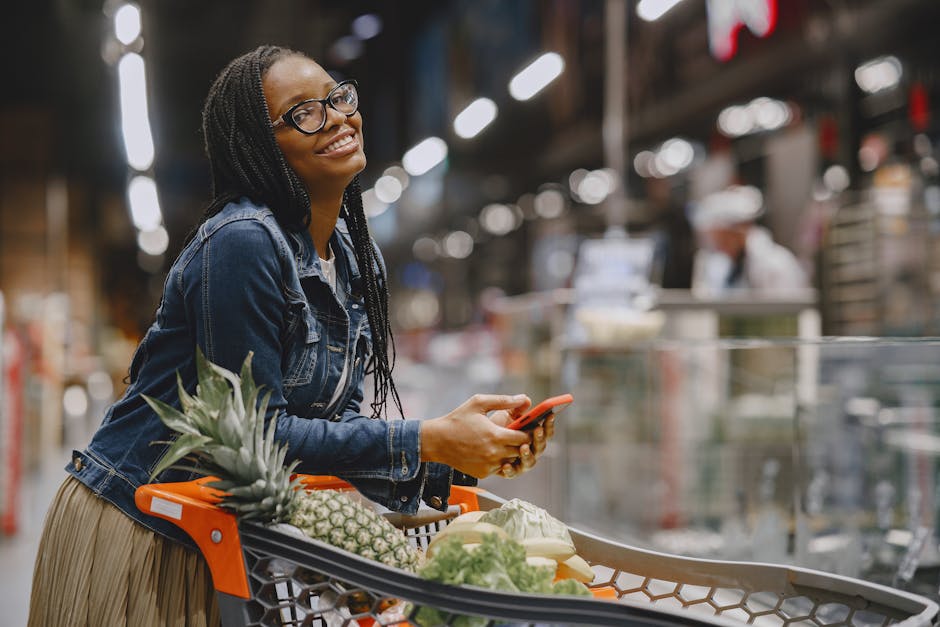 Smiling woman with smartphone shopping in supermarket aisle, using cart.