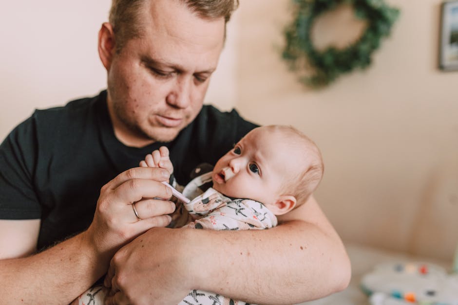A father tenderly checks his baby’s temperature with a thermometer at home.