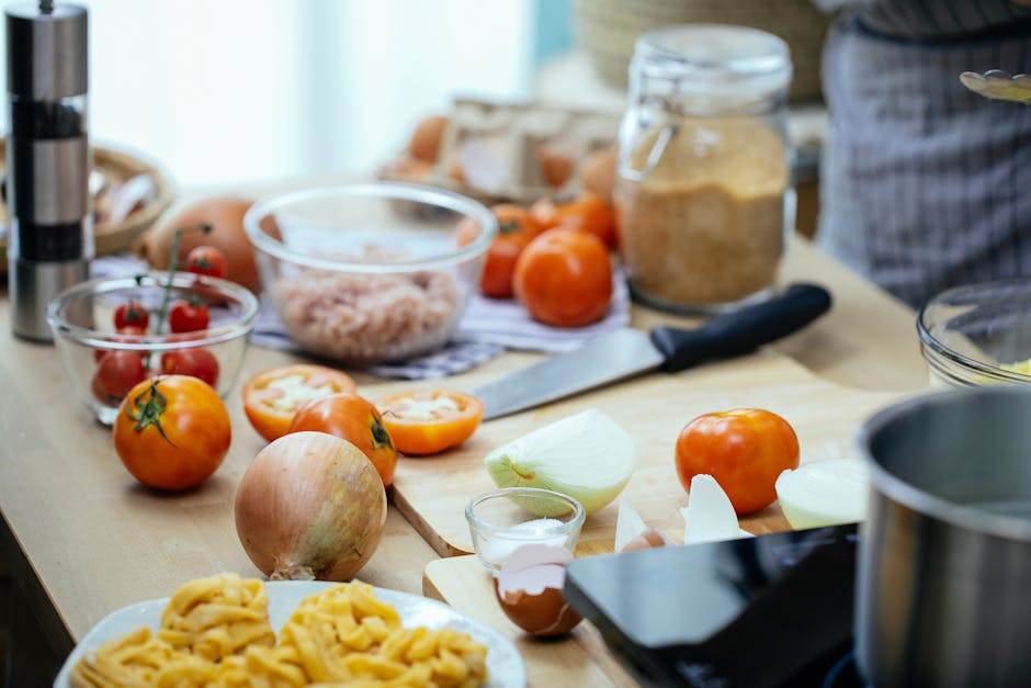 Wooden kitchen countertop with tomatoes and onions and plate of pasta during dinner preparation