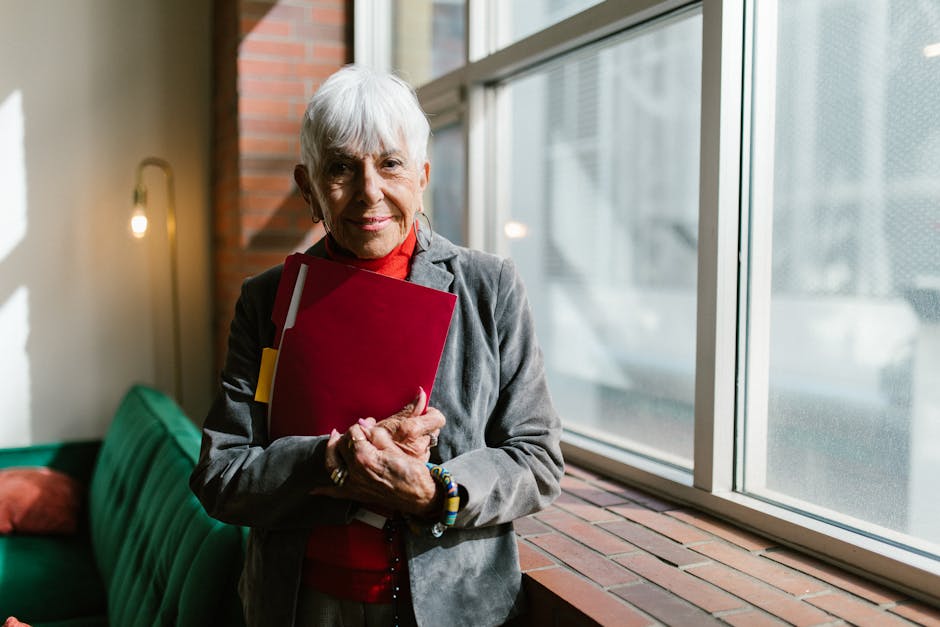 Senior woman holding folder, smiling near a window indoors.