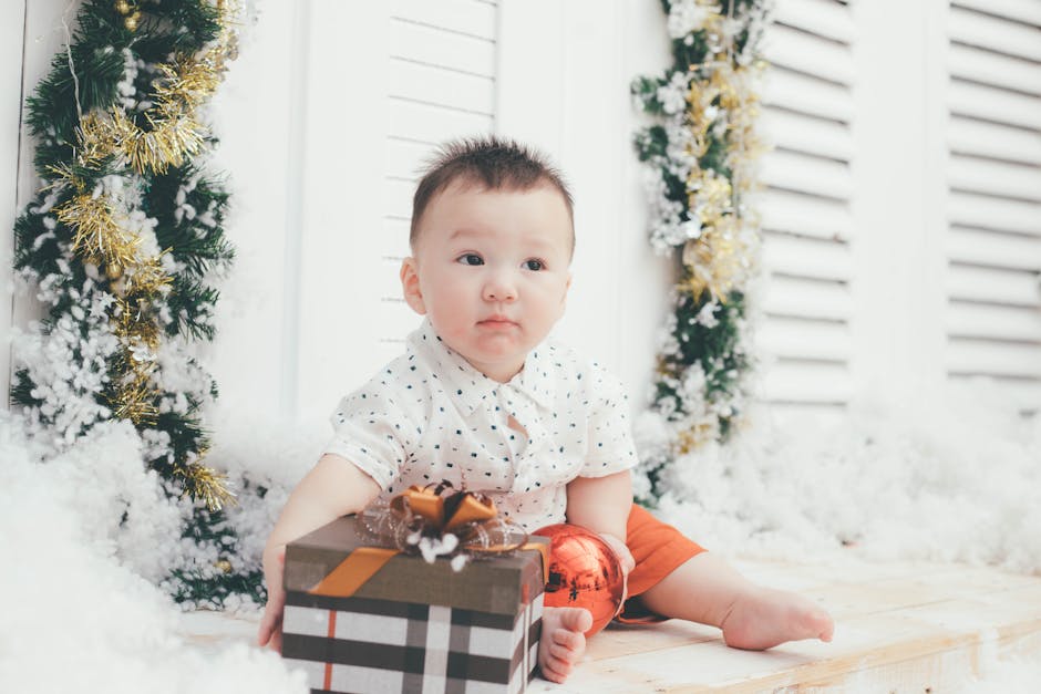 Cute baby sitting indoors with a Christmas gift box, surrounded by festive decorations.