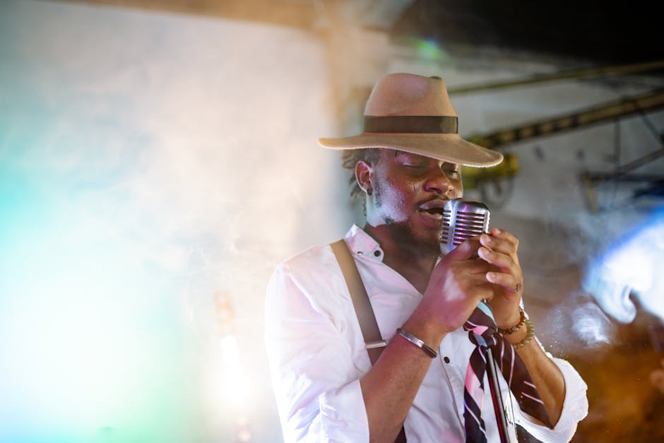 A stylish male singer performs passionately with a vintage microphone and hat on stage.